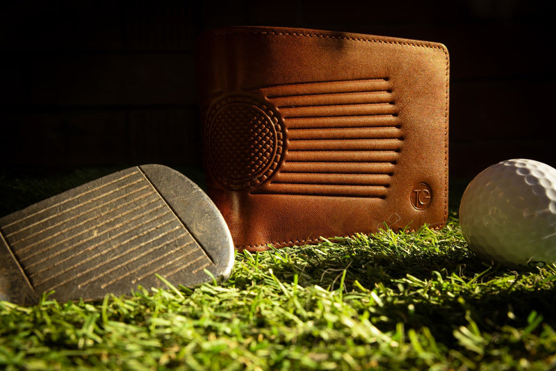Brown leather golf bag with golf club head and ball on grass